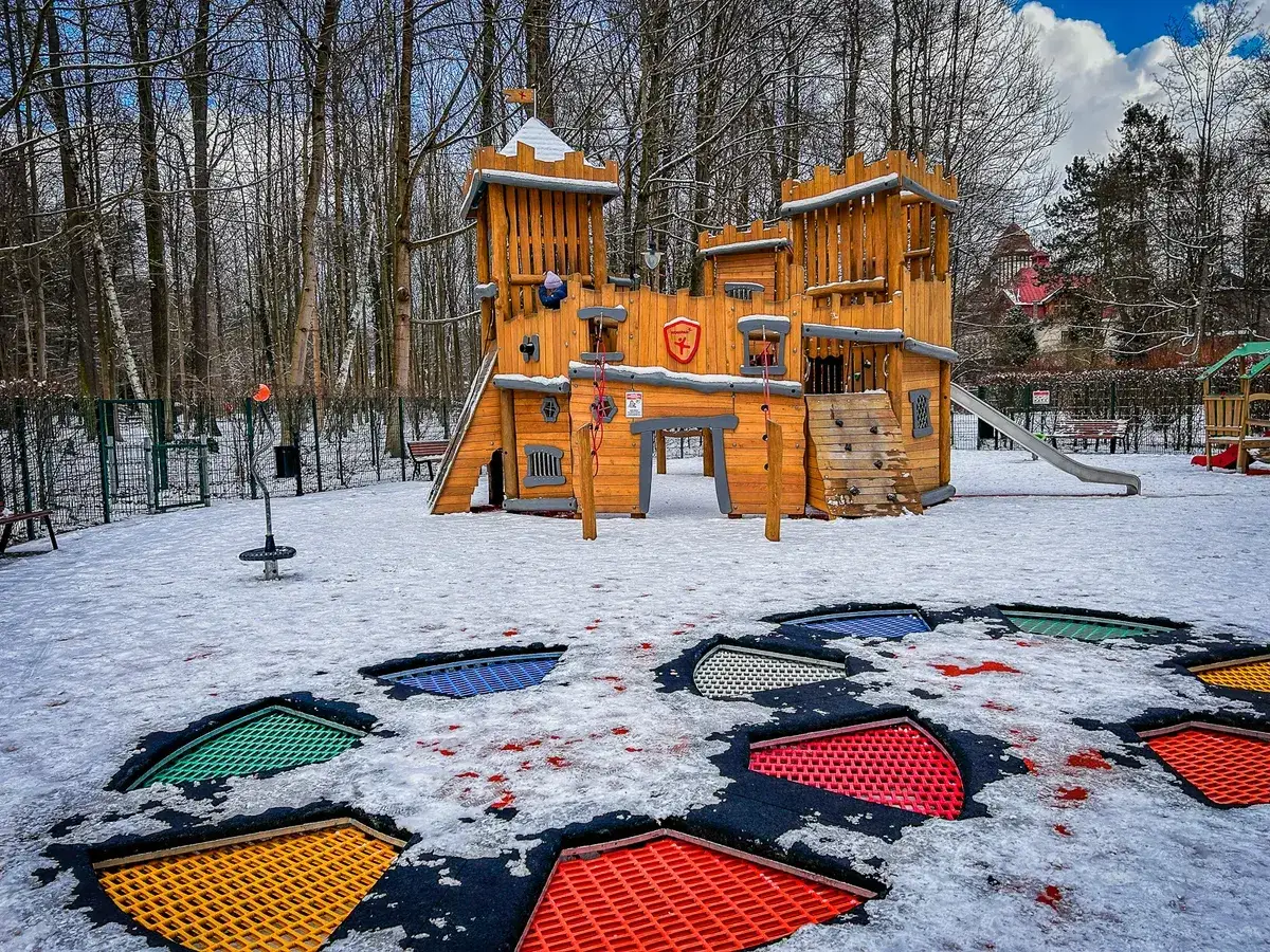 Zimowe atrakcje w Kudowie Zdroju: drewniany zamek na placu zabaw i kolorowe trampoliny w śniegu.