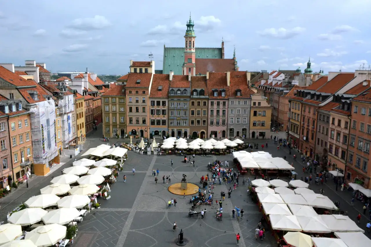 Rynek Starego Miasta w Warszawie, pełen ludzi i białych parasoli kawiarnianych, to jedna z głównych warszawskich atrakcji.